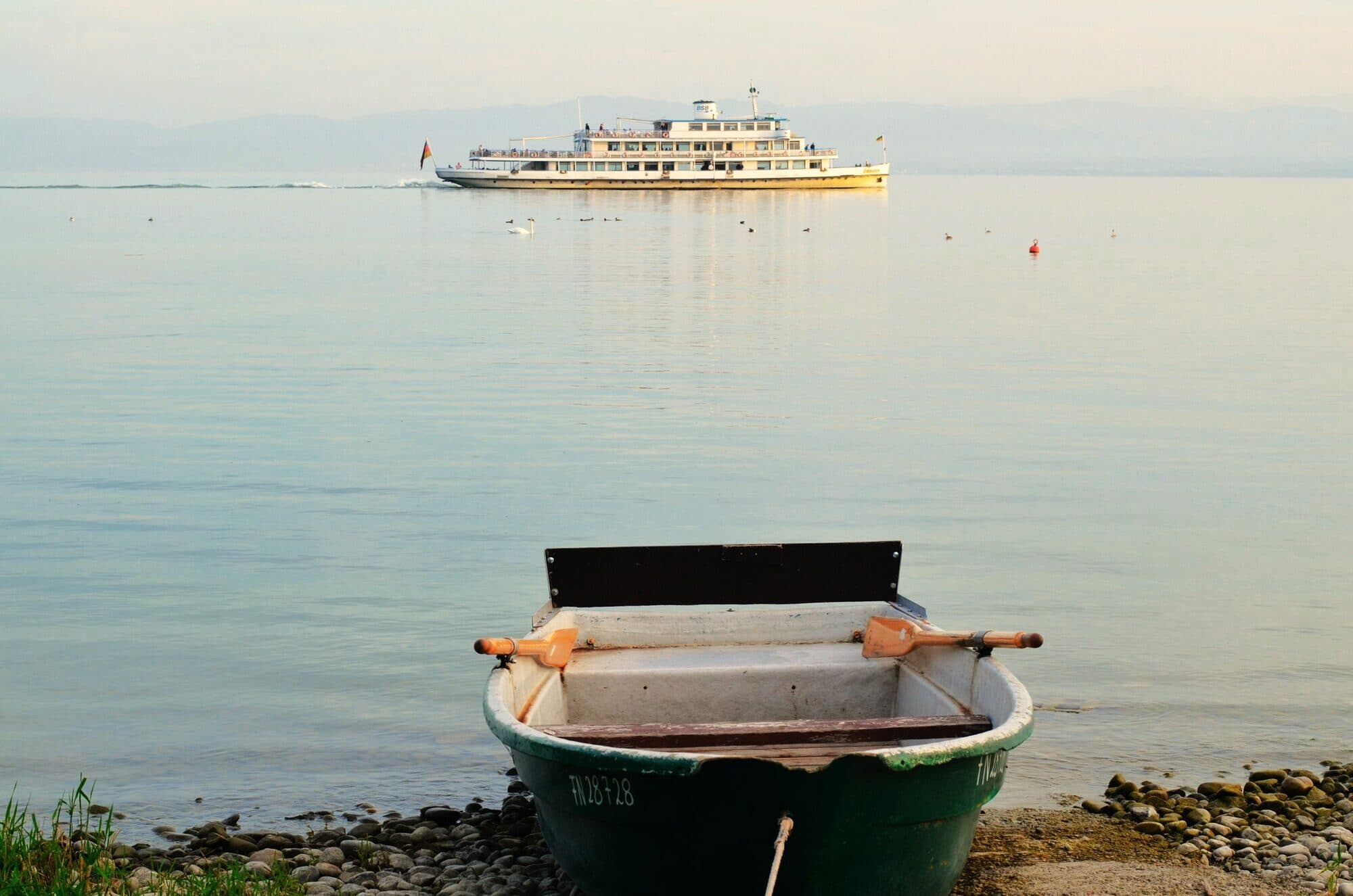 Rowing boat on the shore of Lake Constance, a passenger ship behind it